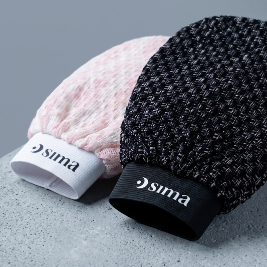 Close-up of pink and black Sima Japanese exfoliating gloves resting on a gray stone surface