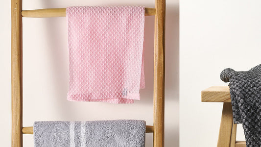 Pink Sima Japanese exfoliating towel hung flat to dry beside a black towel draped over a wooden stool