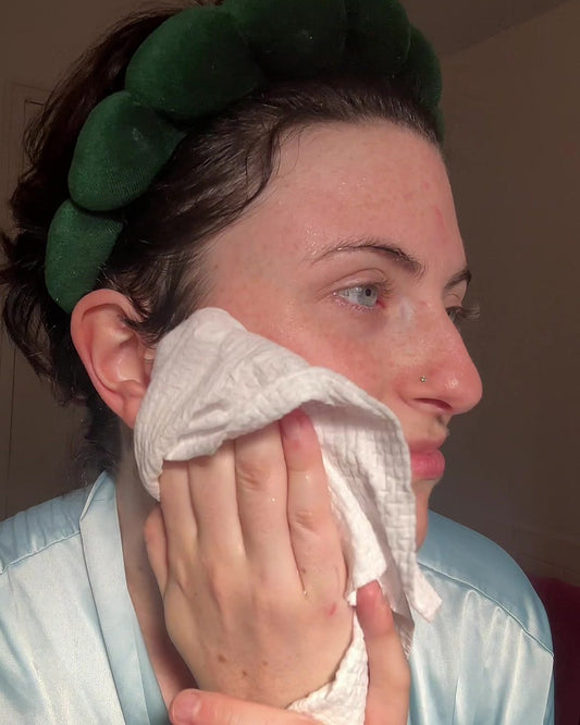 Woman gently pressing a white disposable face towel against her cheek to pat her face dry after washing