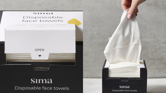 A Sima disposable face towels box with a white lid next to a hand pulling a fresh towel from the same box