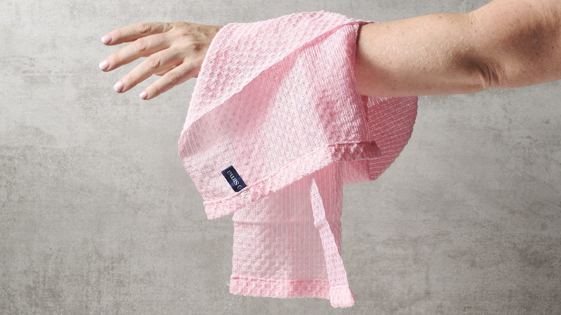 Pink Sima Japanese exfoliating towel draped over an outstretched forearm against a gray wall