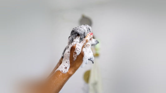 Hand squeezing a lathered Sima exfoliating towel in the shower to build a light foam