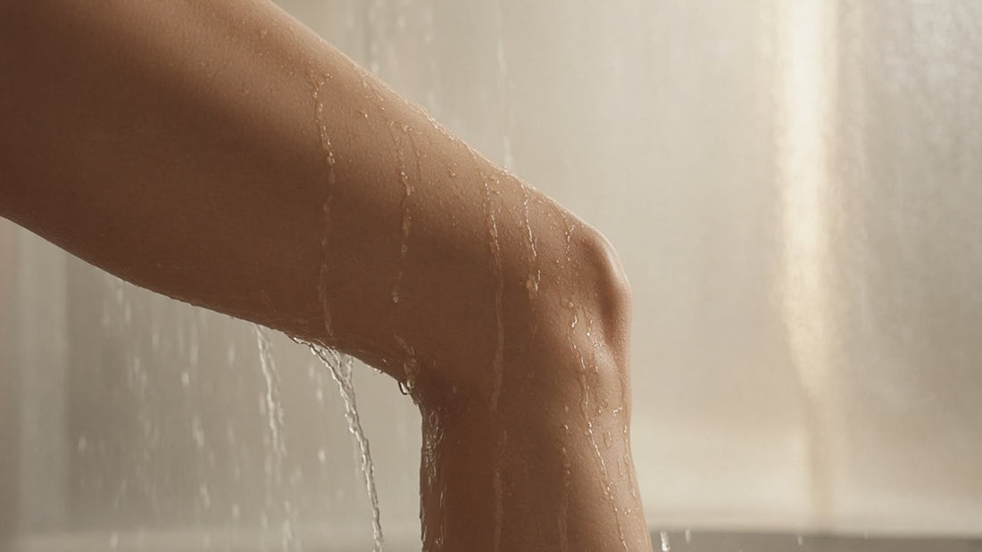 Bent knee and lower thigh in a warm shower with water streaming down the skin