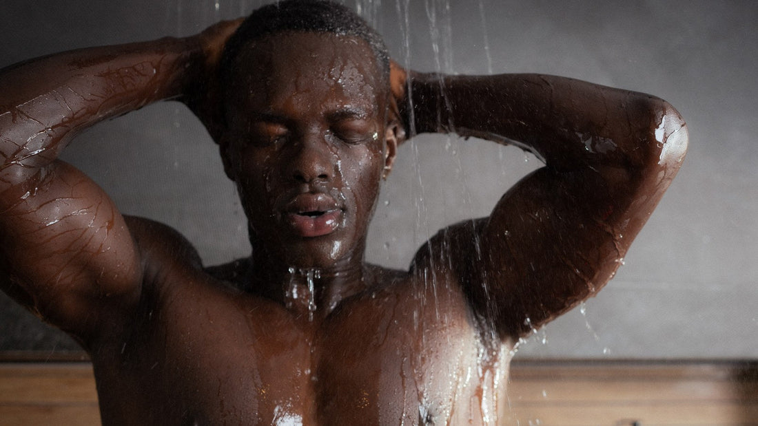 Man rinsing his hair under a running shower, hands on his head
