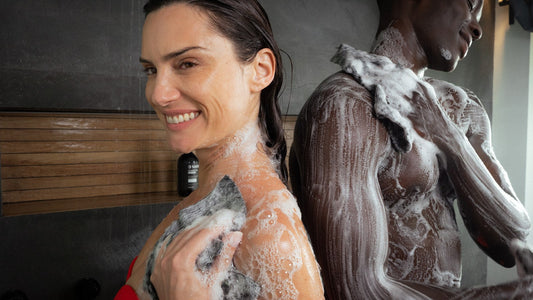 Smiling woman in the shower gently washing her shoulder and upper arm with a dark exfoliating towel