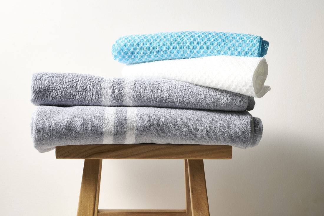 Hand holding a folded gray terry towel with white stripes against a beige background